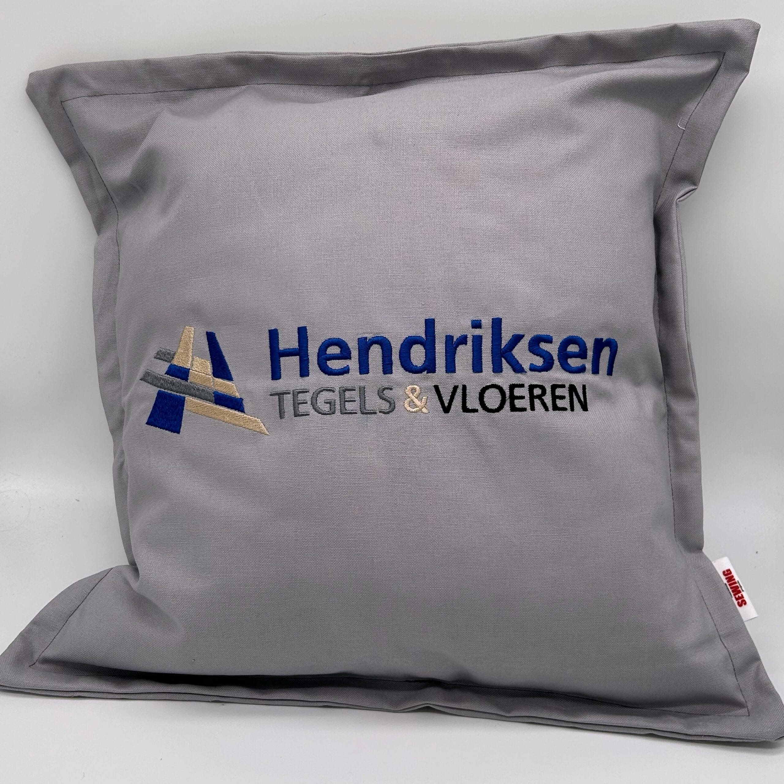 Kussen met logo geborduurd in grijs – professioneel gemaakt in het atelier Rachels Sewing Projects.